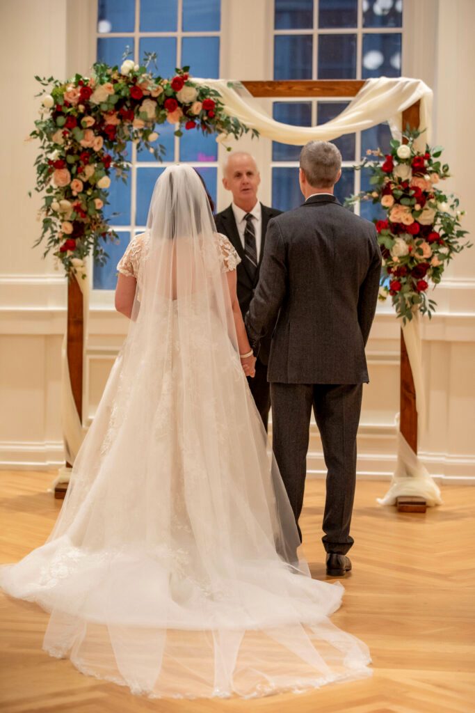 Ralph Griggs officiating a wedding under a burgundy and cream flower arch